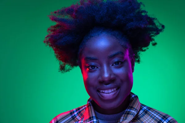 Close-up African young girls portrait on dark green studio background in purple neon light. Afro hairdo. Concept of human emotions — Stock Photo, Image