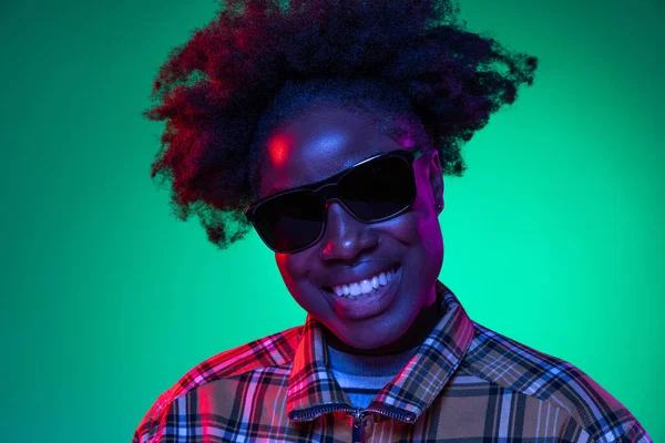 在深绿色工作室背景的紫色霓虹灯下，非洲少女的近照肖像。非洲发式。人类情感的概念 — 图库照片