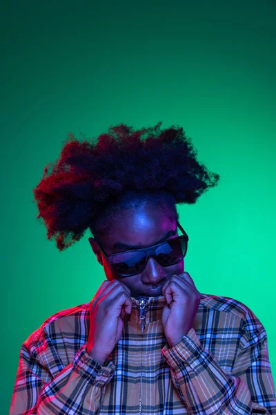 Porträt eines traurigen afrikanischen Mädchens mit Sonnenbrille posiert isoliert auf dunkelgrünem Studiohintergrund in lila Neonlicht. — Stockfoto