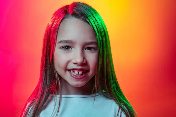 Close-up kleuter meisje, gelukkig kind met lang glanzend haar op zoek naar camera geïsoleerd op rood gele studio achtergrond in neon licht, filter. — Stockfoto