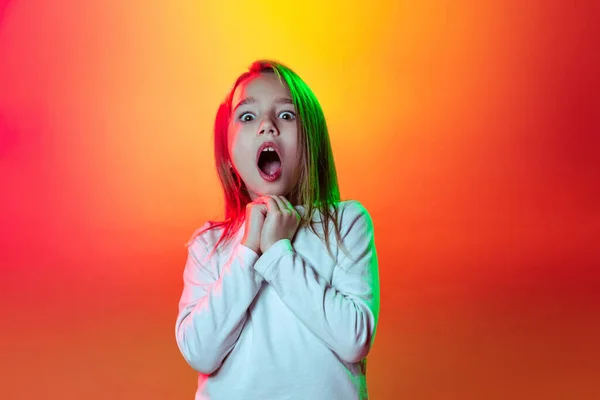 Uma menina surpresa, garoto feliz olhando para a câmera com a boca aberta isolada no fundo do estúdio amarelo vermelho em luz de néon, filtro. — Fotografia de Stock