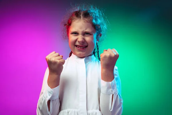 Porträtt av arg liten flicka, barn kopplingar knytnävar isolerad på lutning lila blå färg bakgrund i neon ljus — Stockfoto