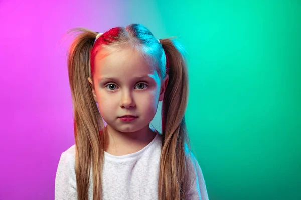 Крупный план дошкольница, спокойный ребенок с длинными глянцевыми волосами глядя на камеру изолированы на градиентном фоне студии в неоновом свете, фильтр. — стоковое фото