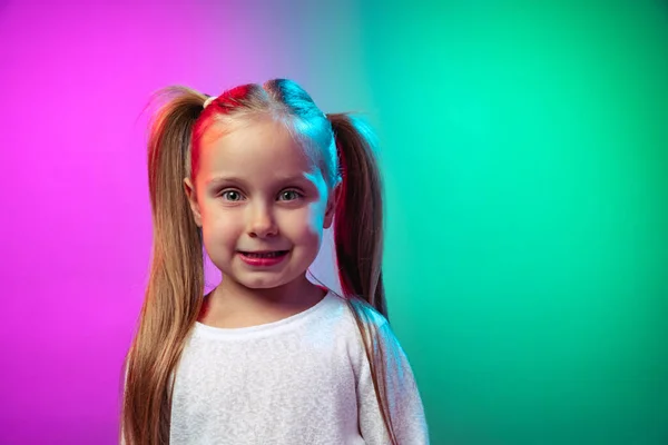 Zbliżenie przedszkola dziewczyna, szczęśliwy dzieciak z długimi, błyszczącymi włosami patrząc na aparat odizolowany na tle gradientowego studia w neonowym świetle, filtr. — Zdjęcie stockowe