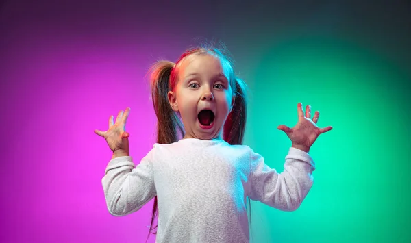 Studio záběr překvapené holčičky, dítě stojící s otevřenými ústy izolované na gradient fialové modré barvy pozadí v neonovém světle — Stock fotografie