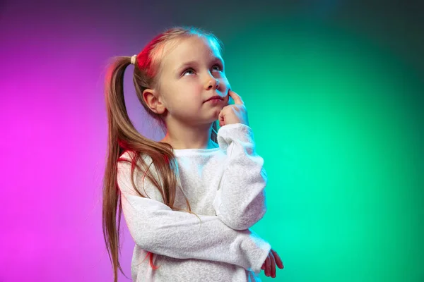 Retrato de media longitud de una niña pensativa soñando aislada sobre fondo de estudio azul púrpura en luz de neón, filtro. — Foto de Stock