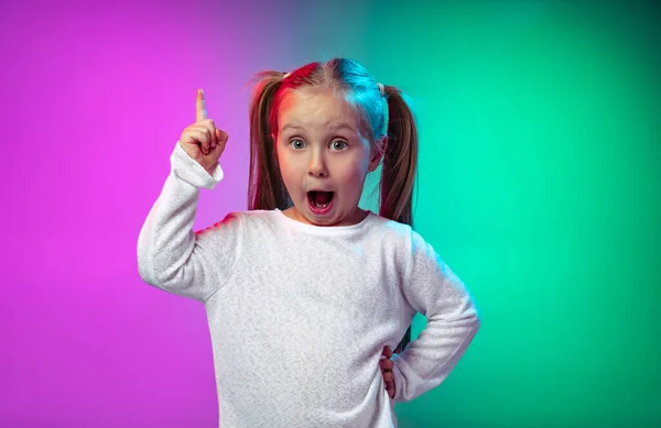 Retrato de pequena menina pré-escolar, garoto bonito levantando o dedo isolado no fundo do estúdio roxo azul em luz de néon, filtro. — Fotografia de Stock