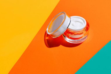 Parlak renkli arka planda markanız için açık cam krema kabı ve fotokopi alanı. Model