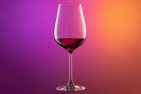 Close-up červené víno sklo izolované přes gradient fialové a oranžové barvy pozadí v neonu. Koncept alkoholu, dovolená, Nový rok — Stock fotografie