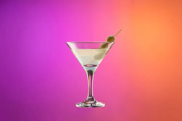 Koktejlové sklo se suchými martini s olivami izolované přes gradient fialové a oranžové barvy pozadí v neonu. — Stock fotografie
