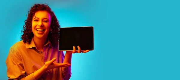 Студійний знімок молодої красивої жінки з планшетом, гаджет ізольований на синьому фоні в неоновому світлі . — стокове фото