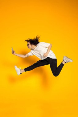 Sarı arka planda izole edilmiş beyaz tişörtlü ve kot pantolonlu genç kızın tam boy portresi..