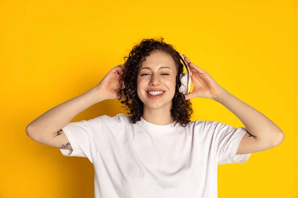 Pandangan depan dari gadis cantik yang tersenyum dengan headphone mendengarkan musik, buku audio yang terisolasi dengan latar belakang kuning — Stok Foto