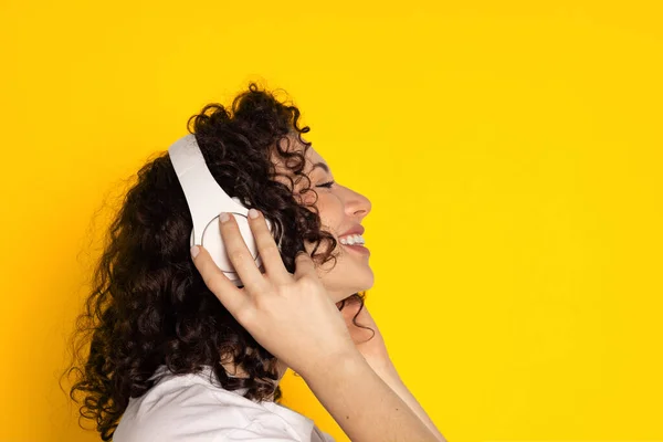 Vista lateral da menina bonita sorrindo em fones de ouvido ouvindo música, livros de áudio isolados no fundo amarelo — Fotografia de Stock