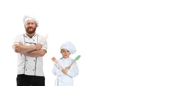 Joven barbudo, cocinero, cocinero de uniforme blanco y su pequeño ayudante, niño posando aislado sobre fondo blanco. — Foto de Stock