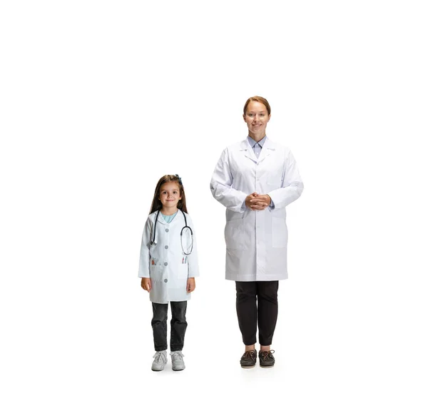Portret van schattig mooi klein meisje, kind in beeld van verpleegkundige en vrouwelijke arts poseren geïsoleerd op witte studio achtergrond — Stockfoto