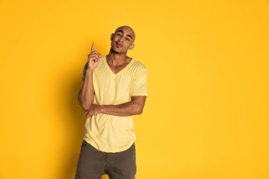 Sarı renkli stüdyo arka planında izole edilmiş duygusal koyu tenli tişörtlü adam pozu. İnsan duyguları kavramı