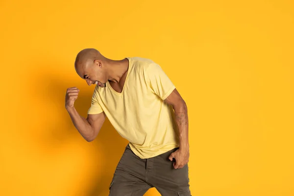 Homem de pele escura emocional em t-shirt posando isolado no fundo do estúdio de cor amarela. Conceito de emoções humanas — Fotografia de Stock