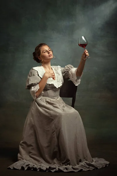 Vintage-Porträt von jungen schönen Mädchen in grauem Kleid mittelalterlichen Stils trinkt Rotwein isoliert auf dunklem Hintergrund. — Stockfoto