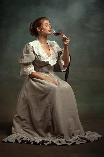穿着中世纪风格灰色衣服的年轻漂亮姑娘的复古画像，她喝着暗色背景下的红酒. — 图库照片