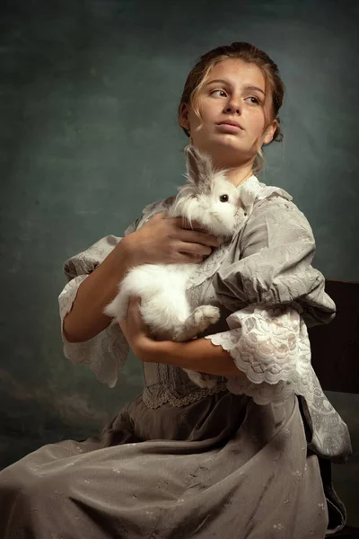 Porträt von jungen schönen Mädchen in grauem Kleid des mittelalterlichen Stils sitzt mit flauschigen Kaninchen isoliert auf dunklem Hintergrund. — Stockfoto