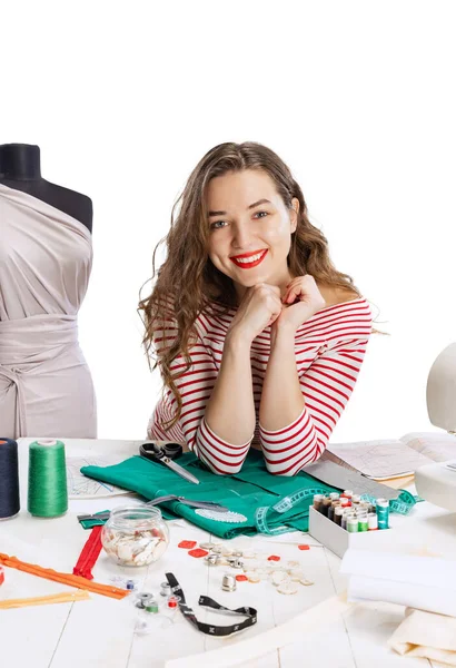 Sonriente linda joven, costurera, modista que trabaja con tela, tijeras y máquina de coser aislada sobre fondo blanco. Concepto de trabajo, hobby — Foto de Stock