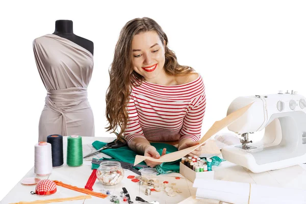 Jovencita hermosa alegre, costurera, modista que trabaja con tela, tijeras y máquina de coser aislada sobre fondo blanco. Concepto de trabajo, hobby — Foto de Stock