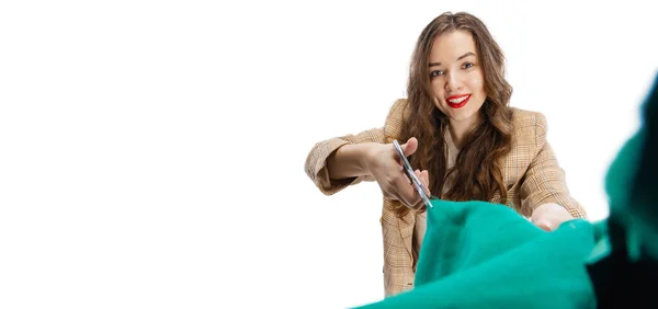 Uśmiechnięta młoda dziewczyna, krawcowa, krawcowa cięcia zielony materiał z nożyczkami izolowane na białym tle. Pojęcie pracy, hobby — Zdjęcie stockowe