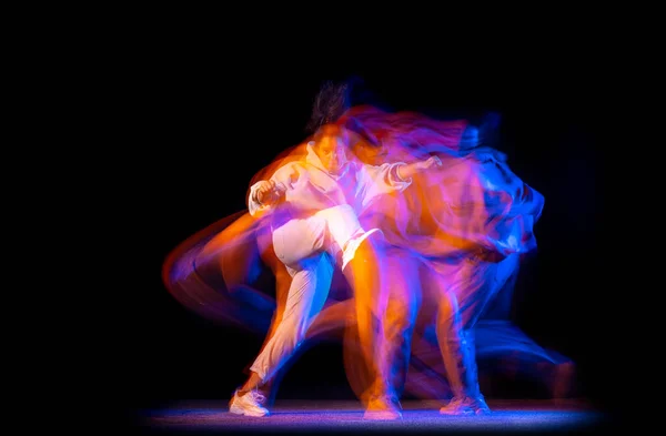 Uma jovem menina esportiva em traje branco dança hip-hop dança isolada no fundo escuro no salão de dança em néon luz mista. — Fotografia de Stock