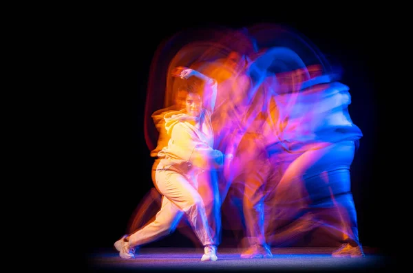 Возбужденная девушка в белом костюме танцует хип-хоп танец на тёмном фоне в танцевальном зале в неоновом смешанном свете. — стоковое фото