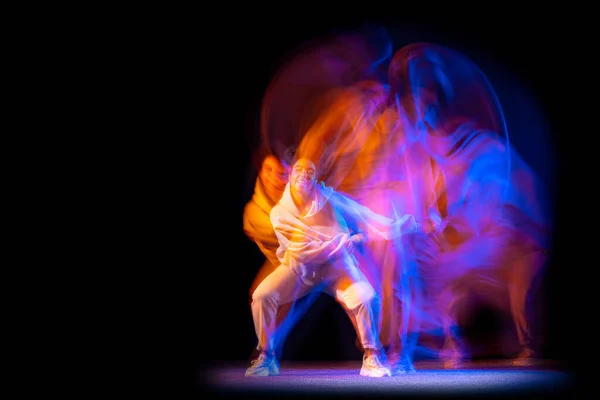 Стильная молодая девушка в белом костюме танцует хип-хоп танцы изолированы на темном фоне в танцевальном зале в неоновом смешанном свете. — стоковое фото