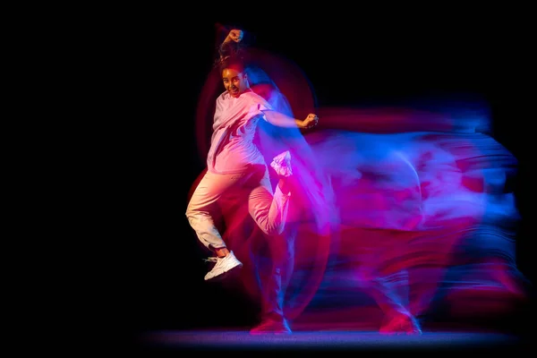 Эмоциональная девушка в белом костюме танцует хип-хоп танец на тёмном фоне в танцевальном зале в неоновом смешанном свете. — стоковое фото