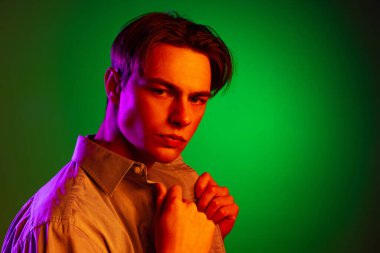 Yakışıklı, ciddi bir adam, yeşil stüdyo arka planında izole edilmiş, tek renkli kameraya bakıyor..