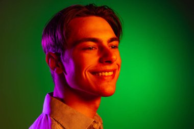 Yeşil stüdyo arka planında izole edilmiş, neon renkli, tek renkli gülümseyen genç adamın yakın çekimi..