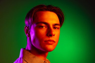 Yakışıklı, ciddi bir adam, yeşil stüdyo arka planında izole edilmiş, tek renkli kameraya bakıyor..