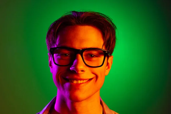 Zbliżenie młodego uśmiechniętego mężczyzny w nowoczesnym okularze odizolowanym na zielonym tle pracowni w neonie, monochromatyczne. — Zdjęcie stockowe