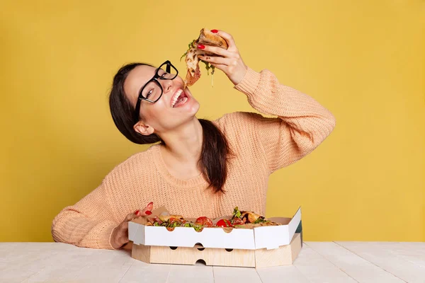 Sarı stüdyo arka planında izole edilmiş lezzetli İtalyan pizzasını tatan neşeli genç kız. Dünya pizza günü — Stok fotoğraf