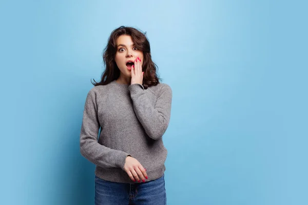 Studio shot of shocked young pretty girl in warm gray knitted sweater posing isolated on blue color background — 图库照片