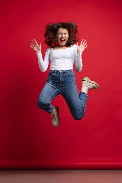 Pełna długość portret podekscytowany młoda piękna dziewczyna w casual ubrania skoki izolowane na czerwonym tle koloru — Zdjęcie stockowe