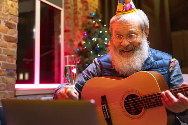 Glücklicher alter bärtiger Mann sitzt zu Hause und feiert seinen Geburtstag mit Freunden und Familie per Videoanruf. — Stockfoto