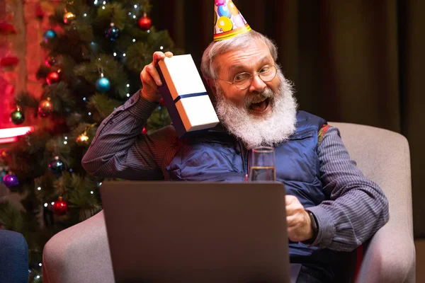 Hombre barbudo viejo emocional sentado en casa y celebra su cumpleaños con amigos y familiares por medio de videollamada. — Foto de Stock