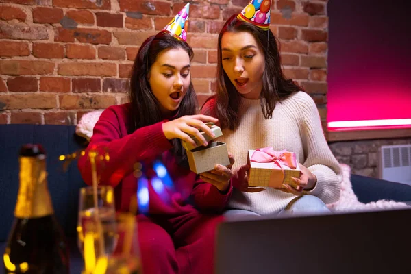 Dos chicas, hermosas amigas sonrientes vistiendo ropa cálida de invierno y sombrero de cumpleaños sentadas en casa y celebrando las vacaciones. —  Fotos de Stock