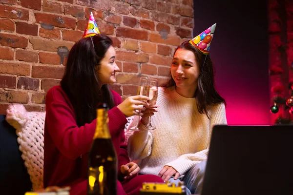 Dos chicas, hermosas amigas sonrientes vistiendo ropa cálida de invierno y sombrero de cumpleaños sentadas en casa y celebrando las vacaciones. —  Fotos de Stock