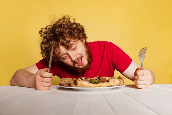 Portrét rudovousého muže připravuje k jídlu lahodnou italskou pizzu izolované na žlutém pozadí studia. — Stock fotografie