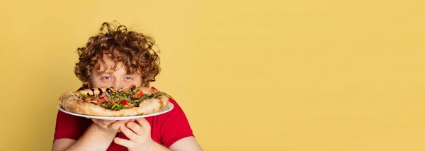 Flyer with young red-bearded man tasting delicious Italian pizza isolated on yellow studio background. — Stock Photo, Image