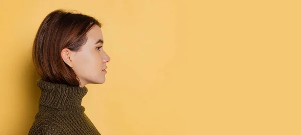 Вид збоку молодої дівчини в теплому темному в'язаному светрі, який виглядає прямо ізольовано на жовтому кольорі. Закрити — стокове фото