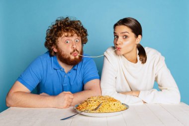 Şirin bir genç adam ve kız birlikte oturup makarna tadıyorlar. Mavi stüdyo arka planında izole edilmiş makarna..