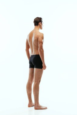 Beyaz stüdyo arka planında tek başına duran, siyah boxer şort giyen genç, yakışıklı, üstsüz, sporcu adamın arka planı..