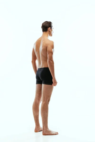 Back view of young handsome shirtless sportive man wearing black boxer-briefs standing isolated on white studio background. — Fotografia de Stock