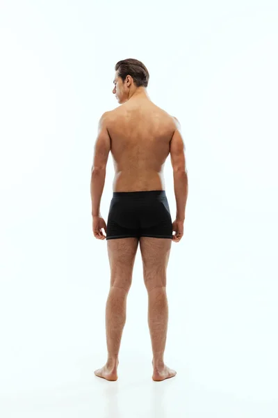 Back view of young handsome shirtless sportive man wearing black boxer-briefs standing isolated on white studio background. — Foto Stock